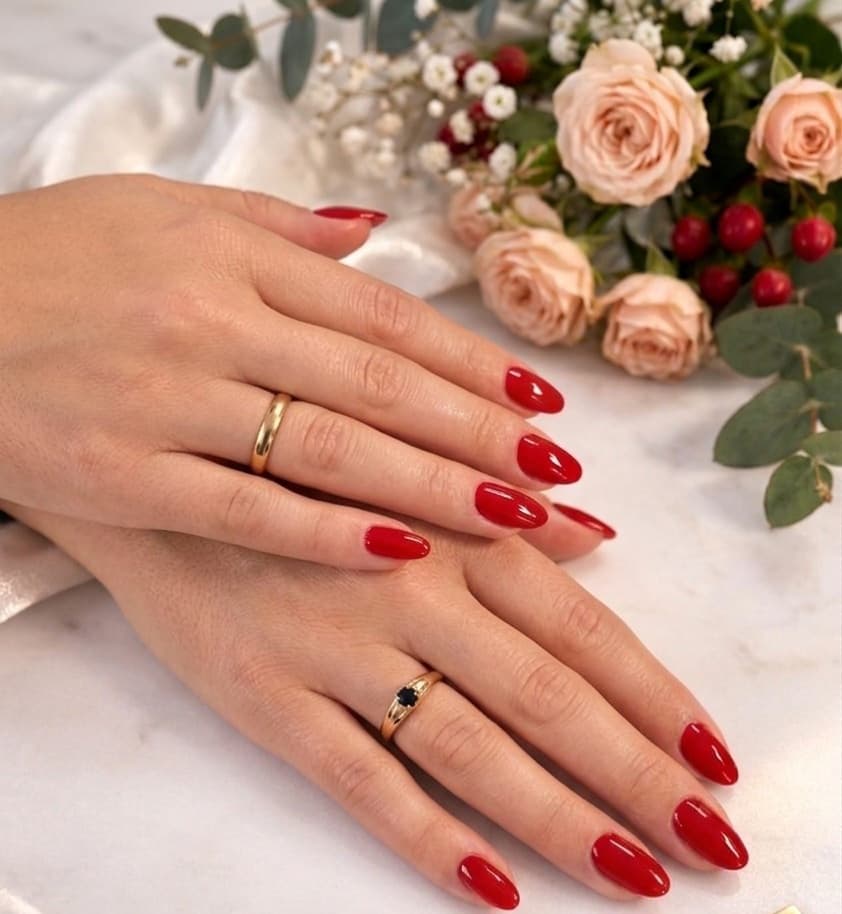Mains aux ongles rouges brillants et bagues dorées devant un bouquet de roses et baies.